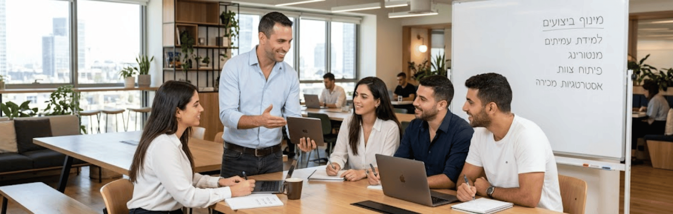 Team of four coworkers around a bright office table as a man stands and presents a tablet to them.